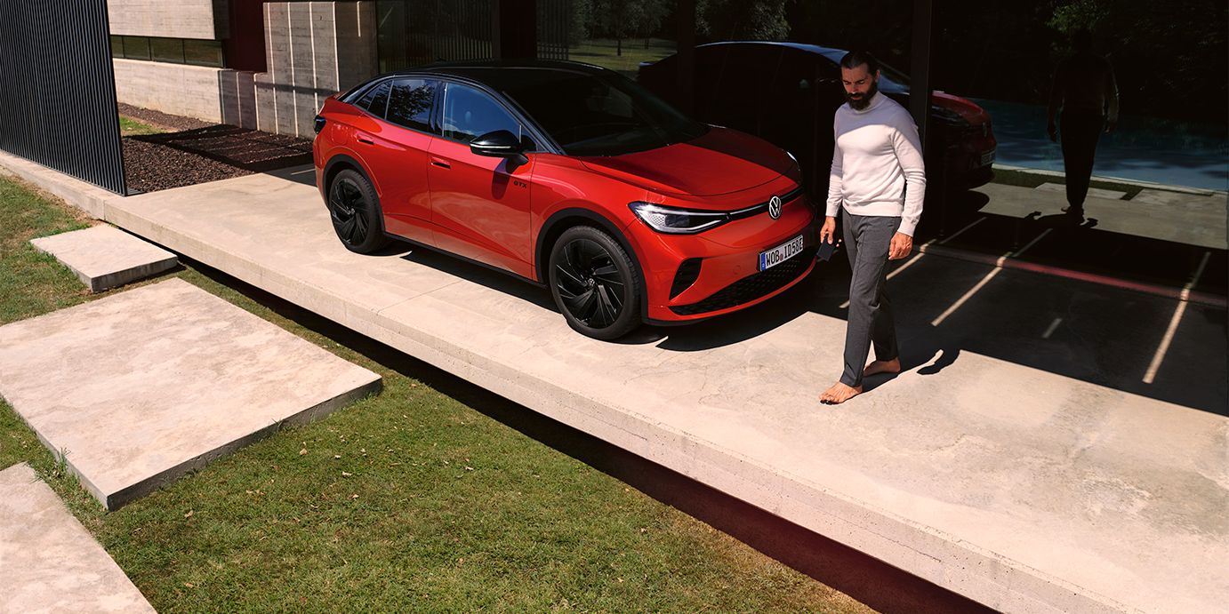 VW ID.5 GTX vermelho visto de dianteira na diagonal num carport moderno, um homem caminha à frente do capot