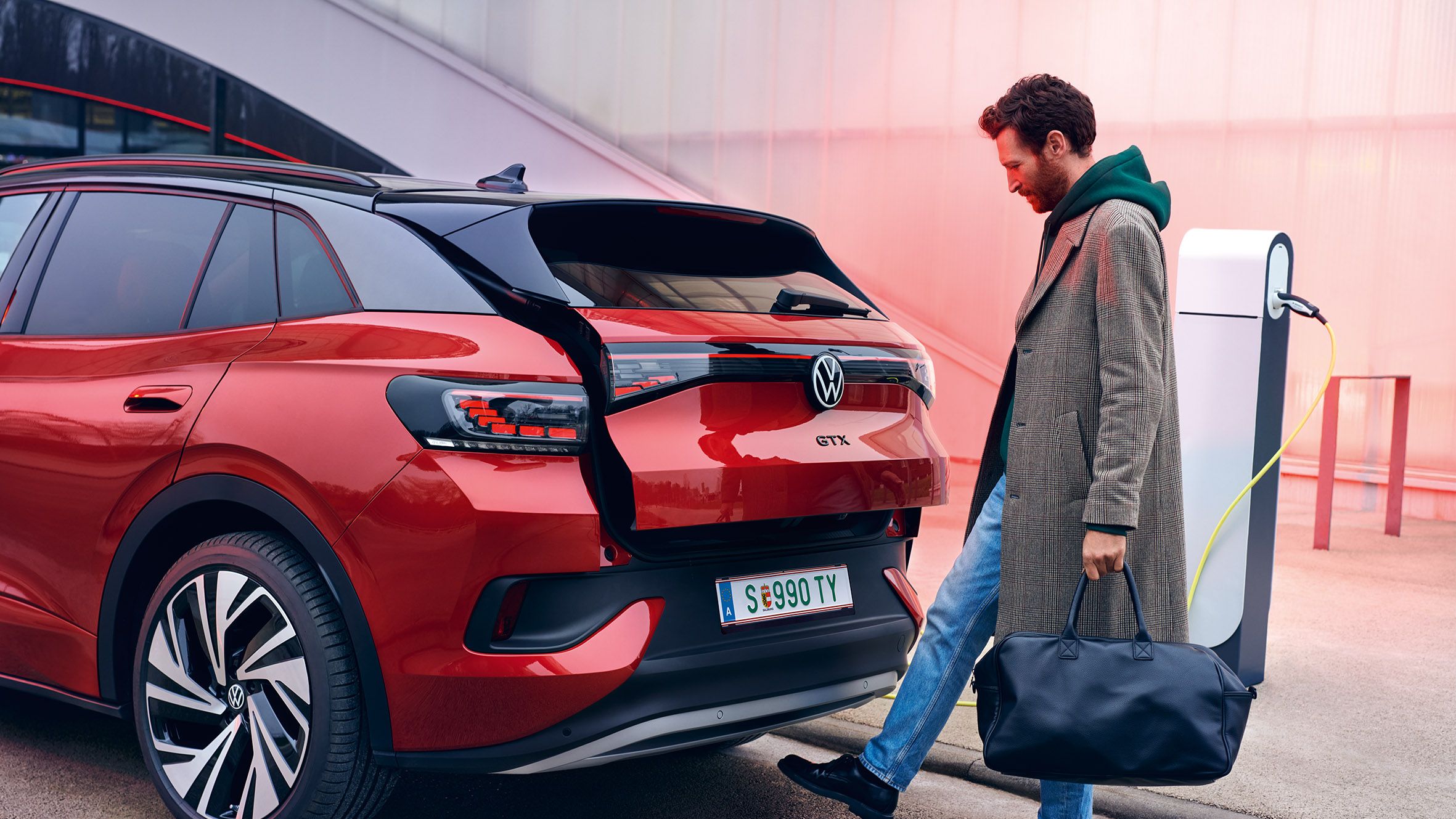 VW ID.4 GTX em vermelho, vista traseira da abertura da bagageira através de sensor, um homem com sacos de compras abre o porta-bagagens.