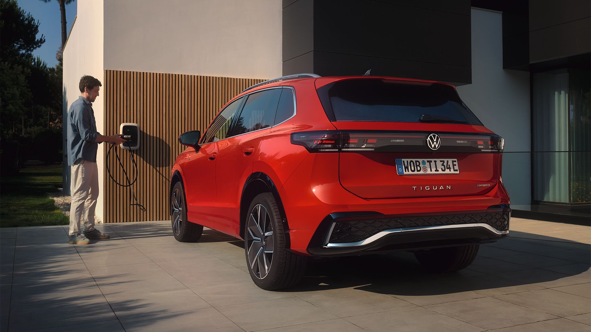 Situação de carregamento de híbrido plug-in: Fotografia traseira do VW Tiguan vermelho estacionado em frente a uma casa. 