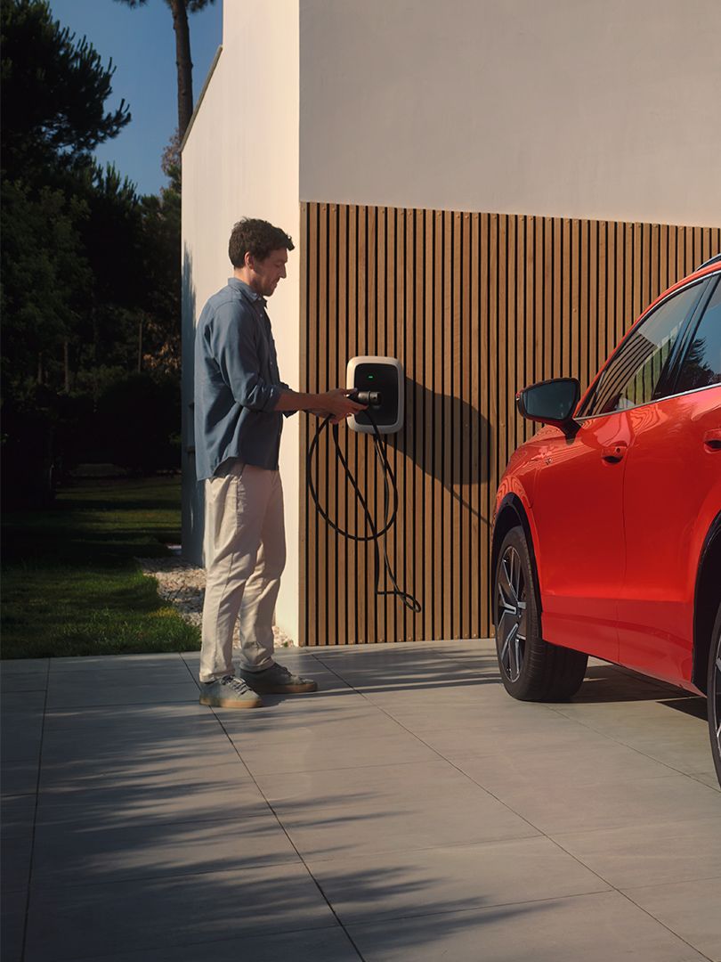 Situação de carregamento de híbrido plug-in: Fotografia traseira do VW Tiguan vermelho estacionado em frente a uma casa. 