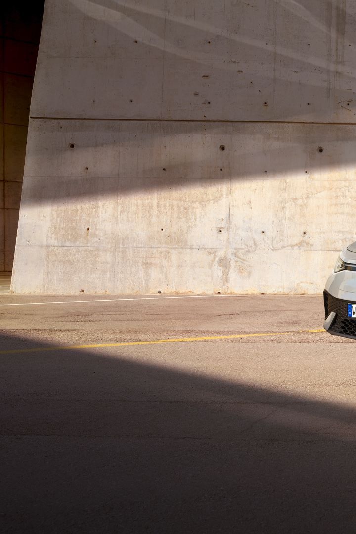 VW ID.5 cinzento estacionado em frente da parede clara de uma casa, vista de frente oblíqua para a direita, um homem dirige-se a passo célere para o automóvel elétrico.