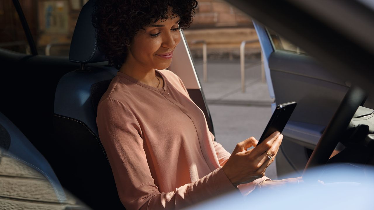 Uma mulher sorridente olha para o telemóvel no banco do condutor de um VW T-Cross estacionado.