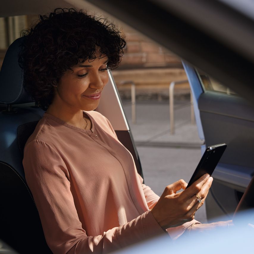 Uma mulher sorridente olha para o telemóvel no banco do condutor de um VW T-Cross estacionado.