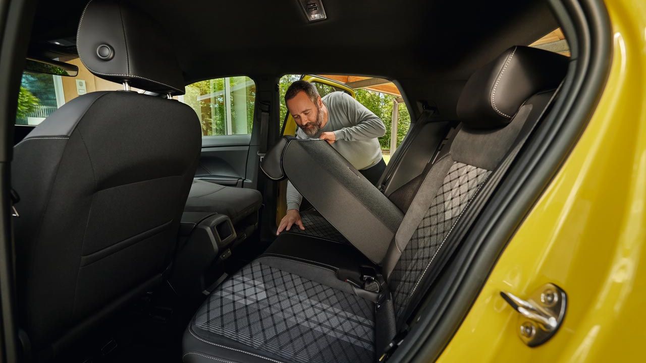 Um homem rebate o banco traseiro de um VW T-Cross amarelo para a frente.