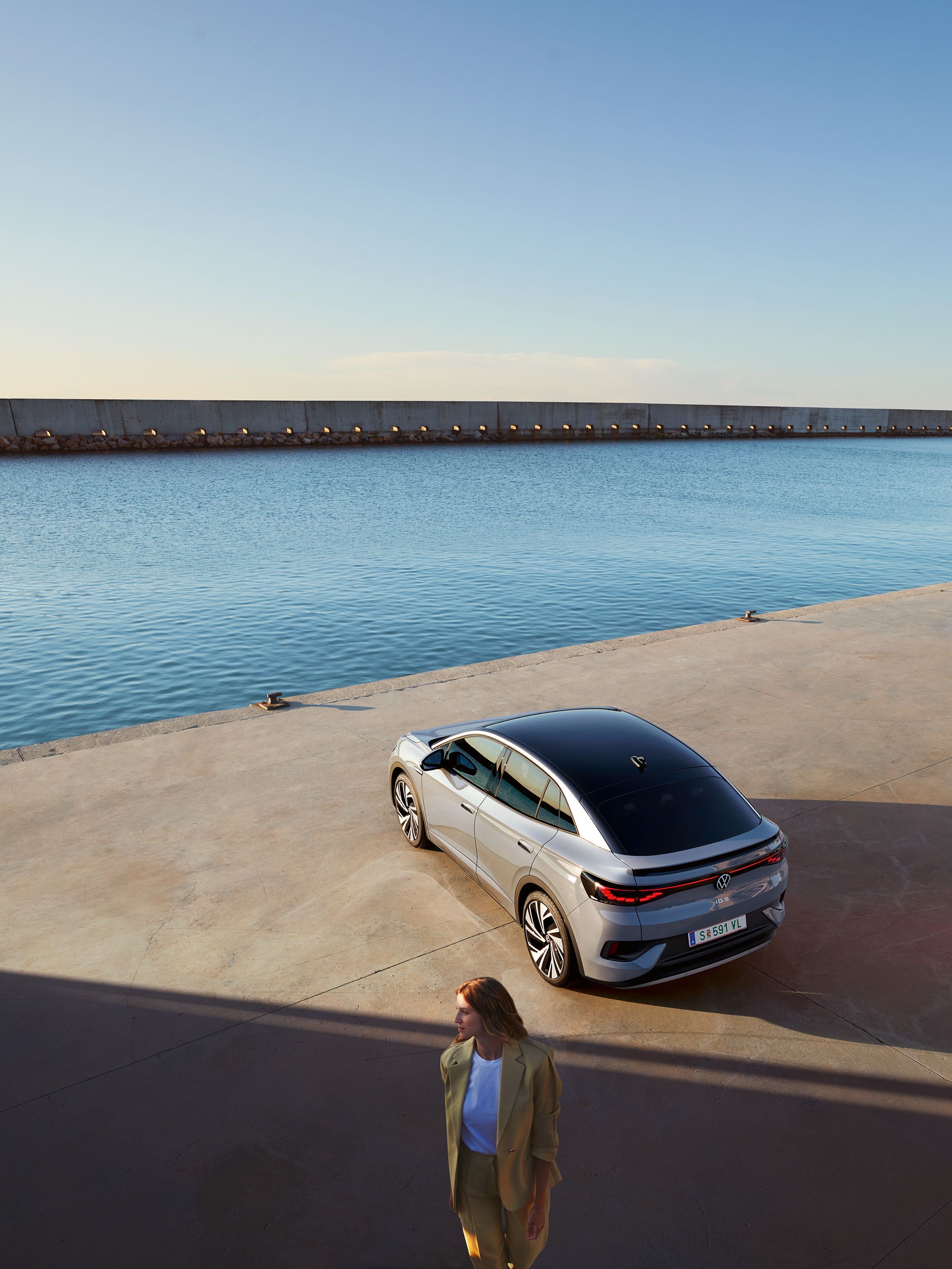 Vista superior oblíqua da traseira de um VW ID.5 no cais de um porto, em primeiro plano vê-se uma mulher