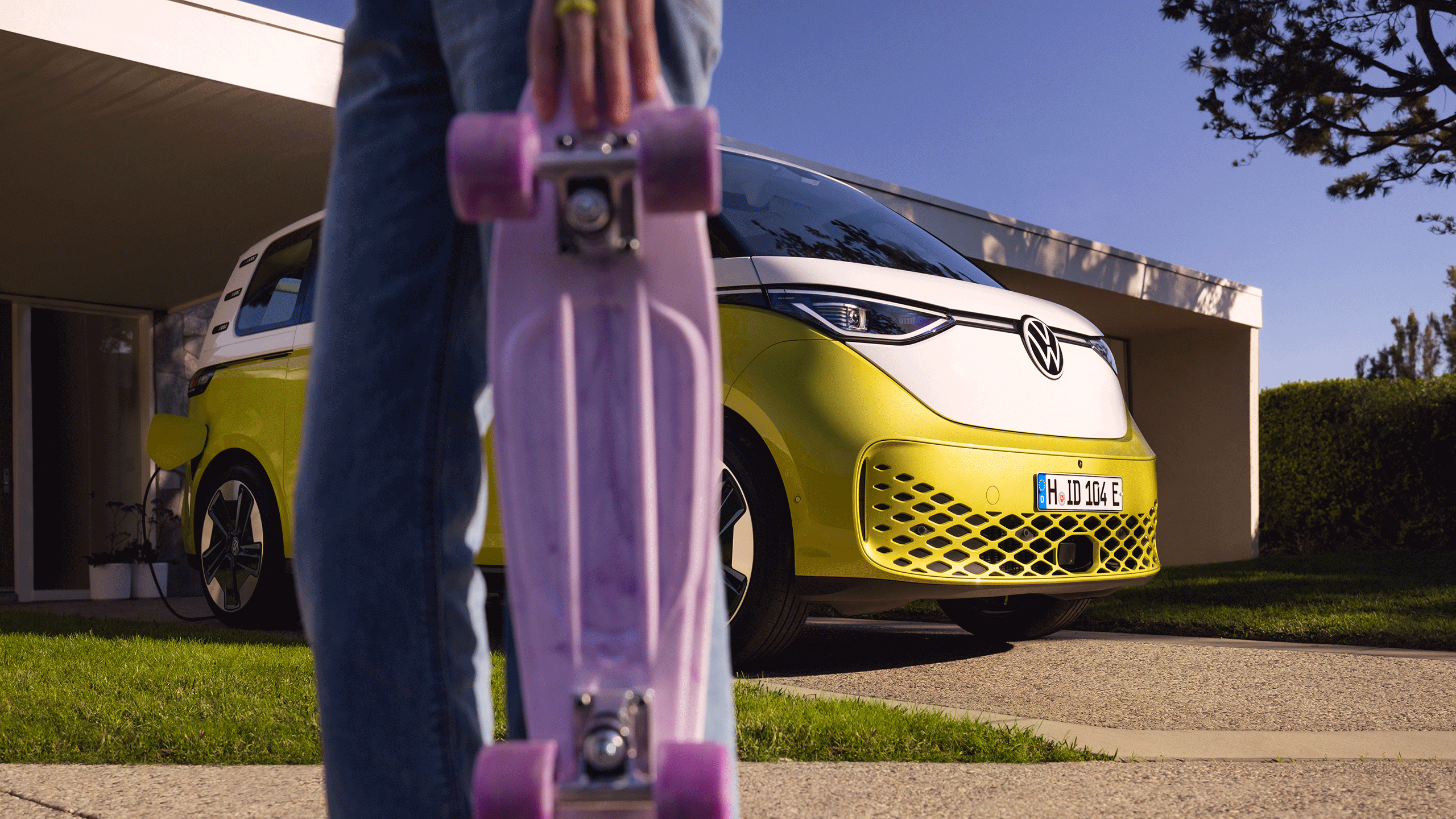 O ID. Buzz estacionado em frente de um acesso; em primeiro plano uma rapariga com uma prancha de skate roxa. 