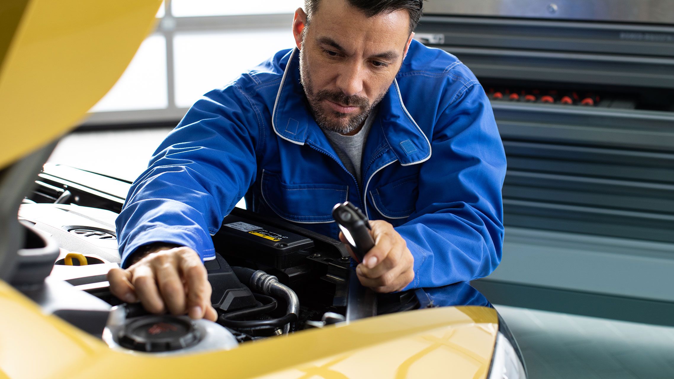 Um funcionário da VW verifica os fluidos de um veículo VW amarelo durante o controlo do veículo numa oficina.