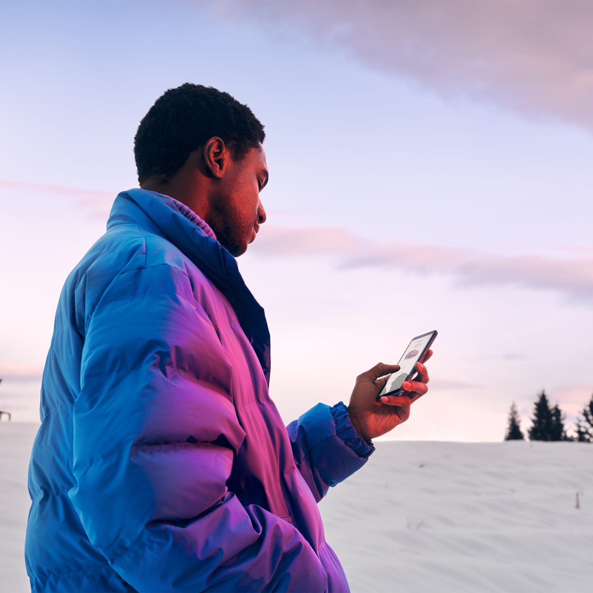 Um homem com casaco de inverno numa paisagem de neve a olhar para o seu smartphone.