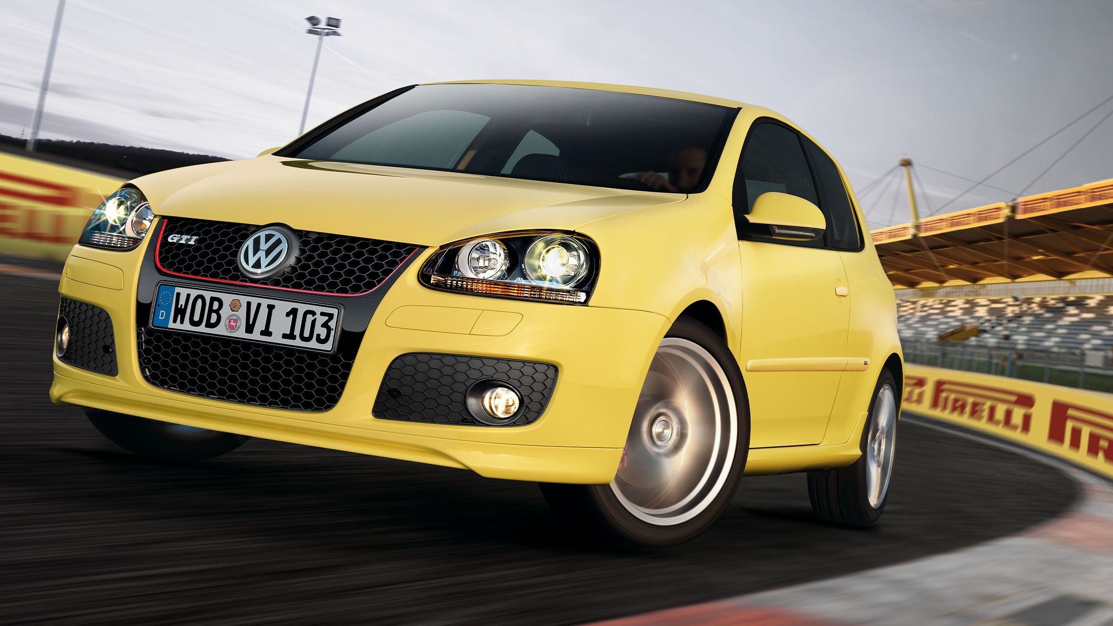 Um Volkswagen Golf 5 GTI amarelo numa pista de corridas com publicidade da Pirelli ao fundo