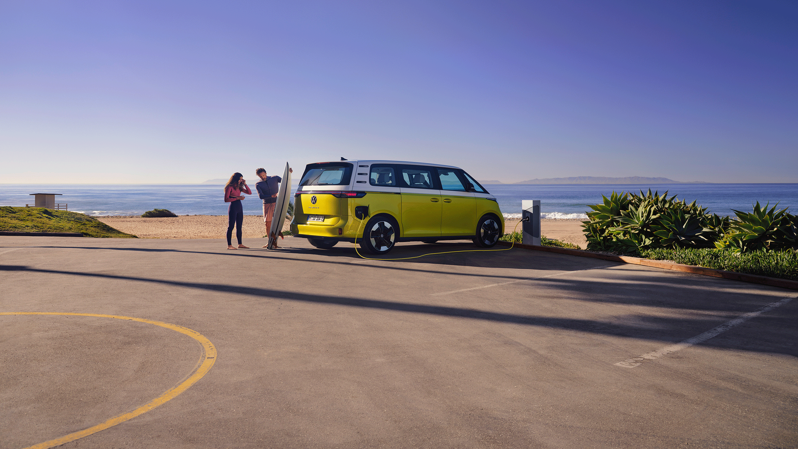 O VW ID. Buzz estacionado na praia, um homem mostra uma prancha de surf à filha.