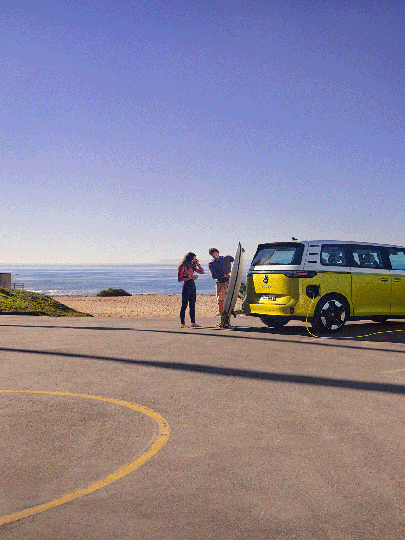 O VW ID. Buzz estacionado na praia, um homem mostra uma prancha de surf à filha.