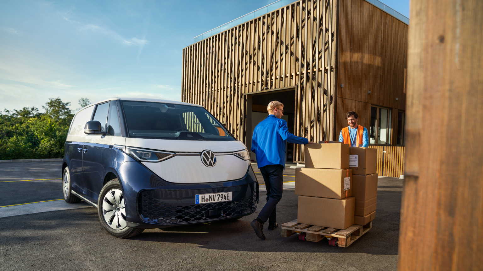 Uma mulher e um homem carregam um ID. Buzz Cargo, o Transporter elétrico da Volkswagen, azul e branco. 