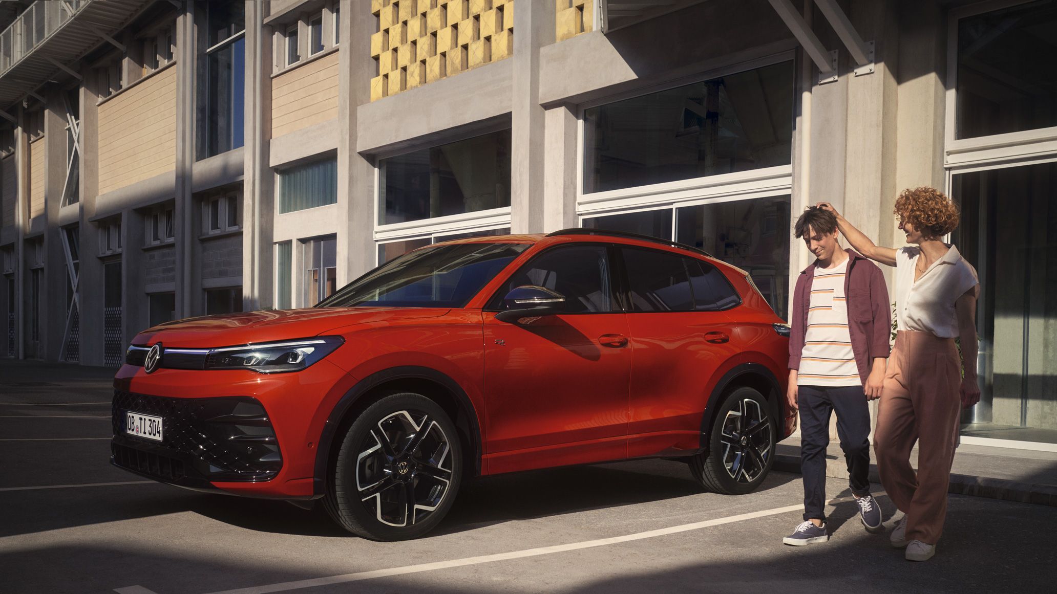 VW Tiguan vermelho estacionado em frente a um edifício, com uma mulher e um adolescente a caminharem ao lado.