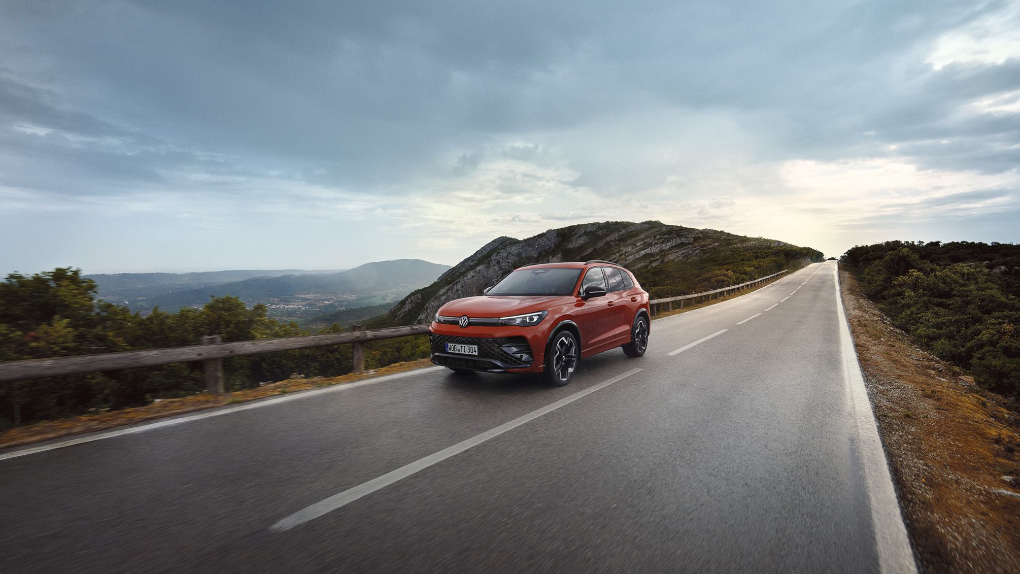 O VW Tiguan vermelho desloca-se ao longo de uma estrada.