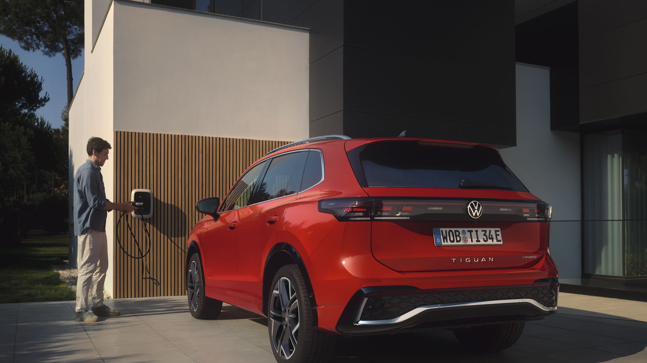 Situação de carregamento de híbrido plug-in: Fotografia traseira do VW Tiguan vermelho estacionado em frente a uma casa. 