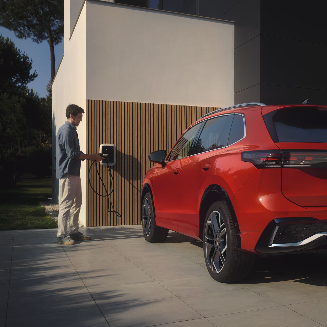 Situação de carregamento de híbrido plug-in: Fotografia traseira do VW Tiguan vermelho estacionado em frente a uma casa. 