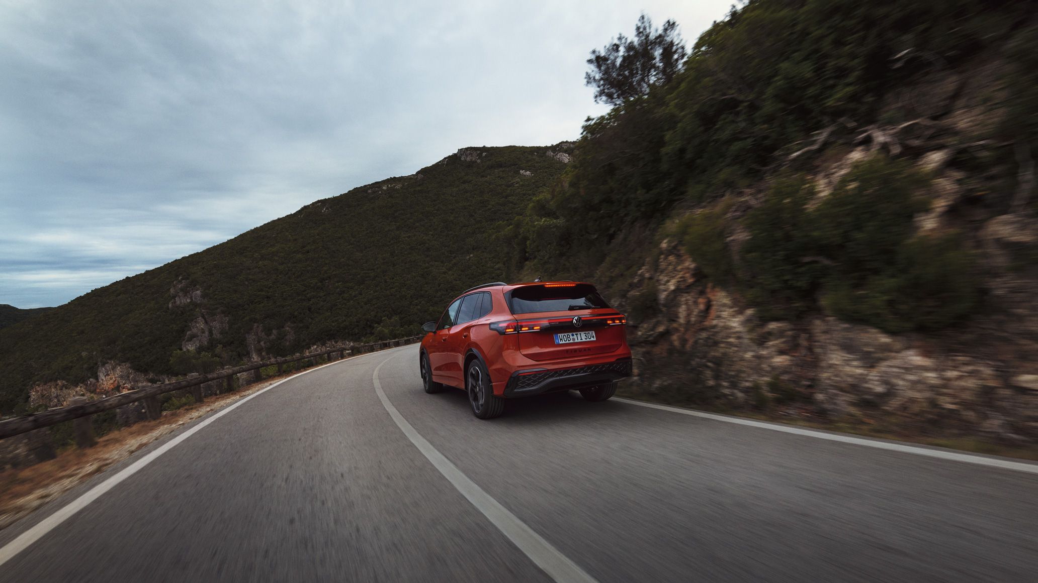 Vista traseira de um VW Tiguan vermelho a atravessar uma paisagem montanhosa.