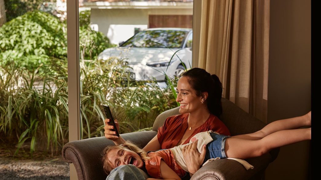 Eine Frau mit ihrer Tochter auf einem Sofa, die Frau blickt auf ihr Smartphone