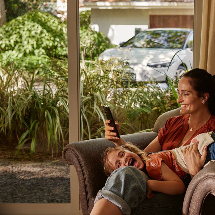 Eine Frau mit ihrer Tochter auf einem Sofa, die Frau blickt auf ihr Smartphone