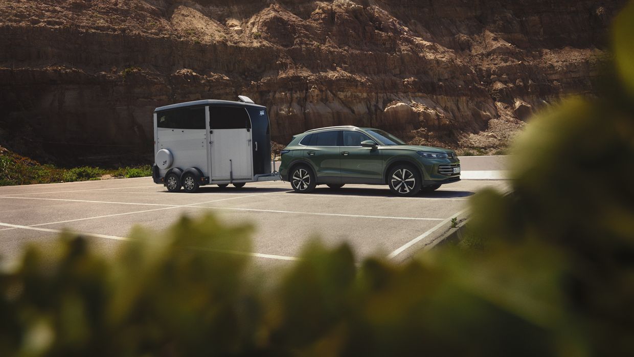 VW Tiguan verde escuro com reboque para cavalos estacionado diante de uma paisagem rochosa.