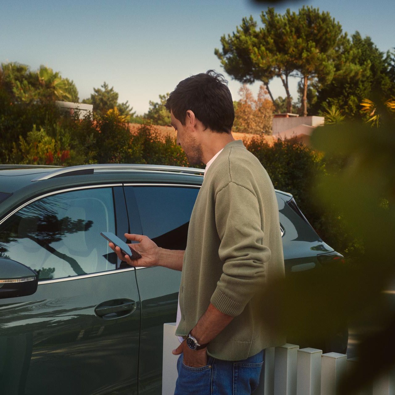 Um jovem no lado do condutor do VW Tiguan verde escuro opera o Park Assist Plus opcional através do seu smartphone.