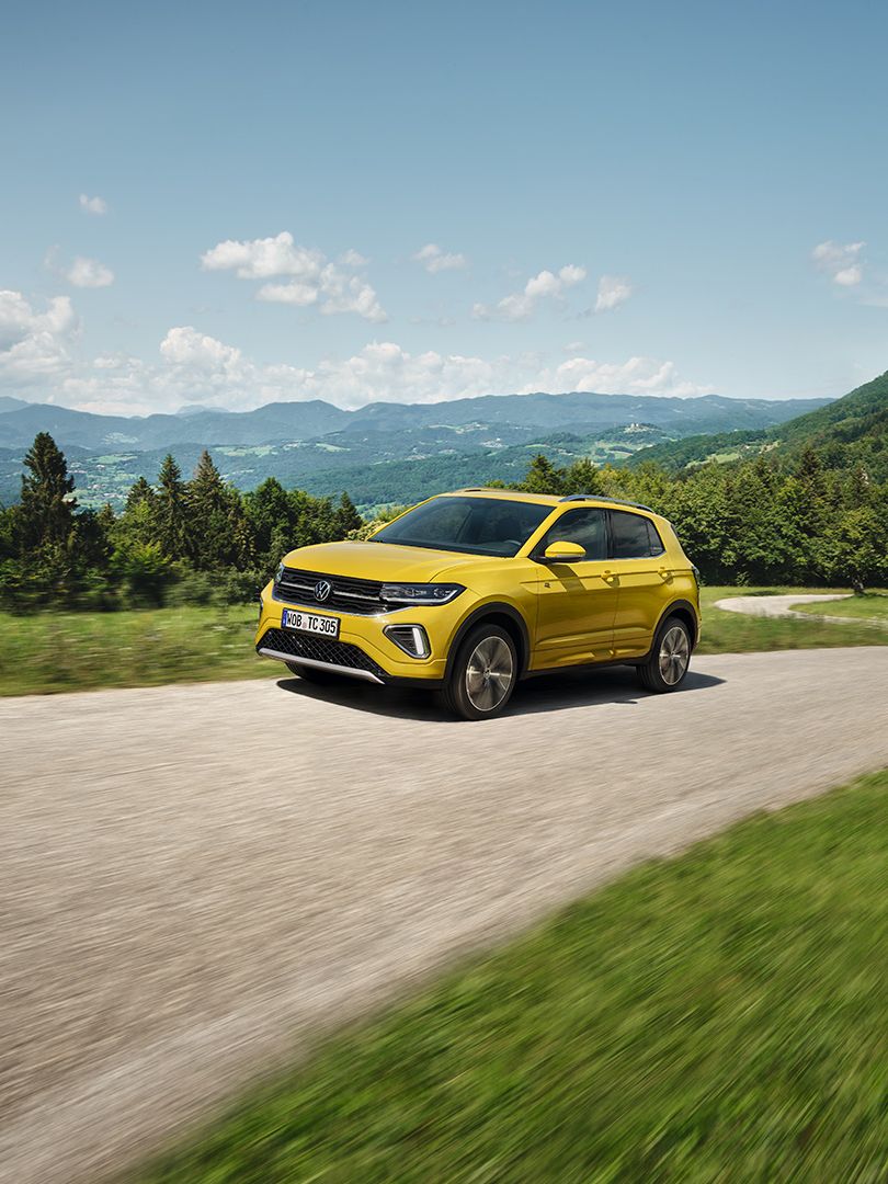 Um VW T-Cross amarelo numa estrada com paisagem montanhosa.