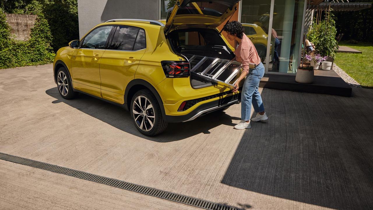 Uma jovem empurra uma escada para a bagageira de um VW T-Cross amarelo.