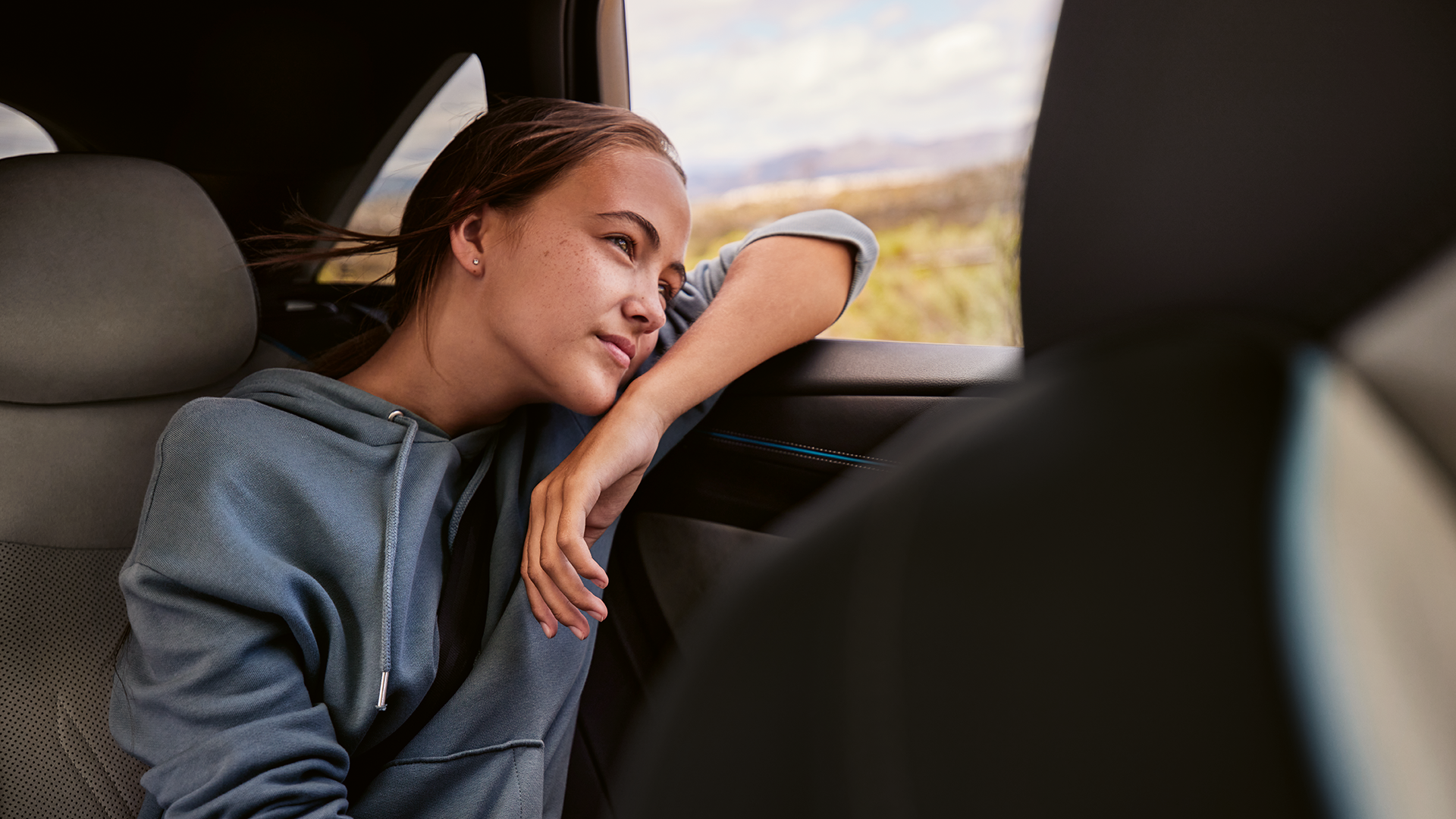 Mulher jovem no banco traseiro de um VW ID.7 olhando para fora da janela.