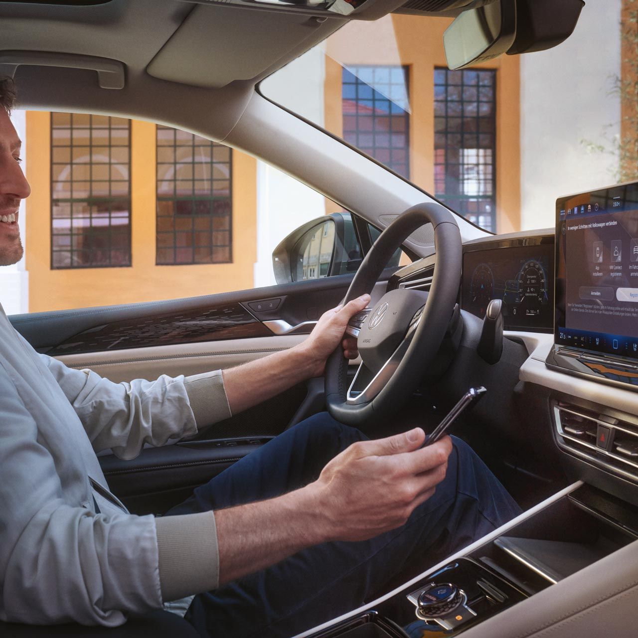 Fotografia do interior de um VW Tiguan. Um homem sentado no banco do condutor utiliza o seu smartphone para controlar a aplicação VW Connect Plus opcional.