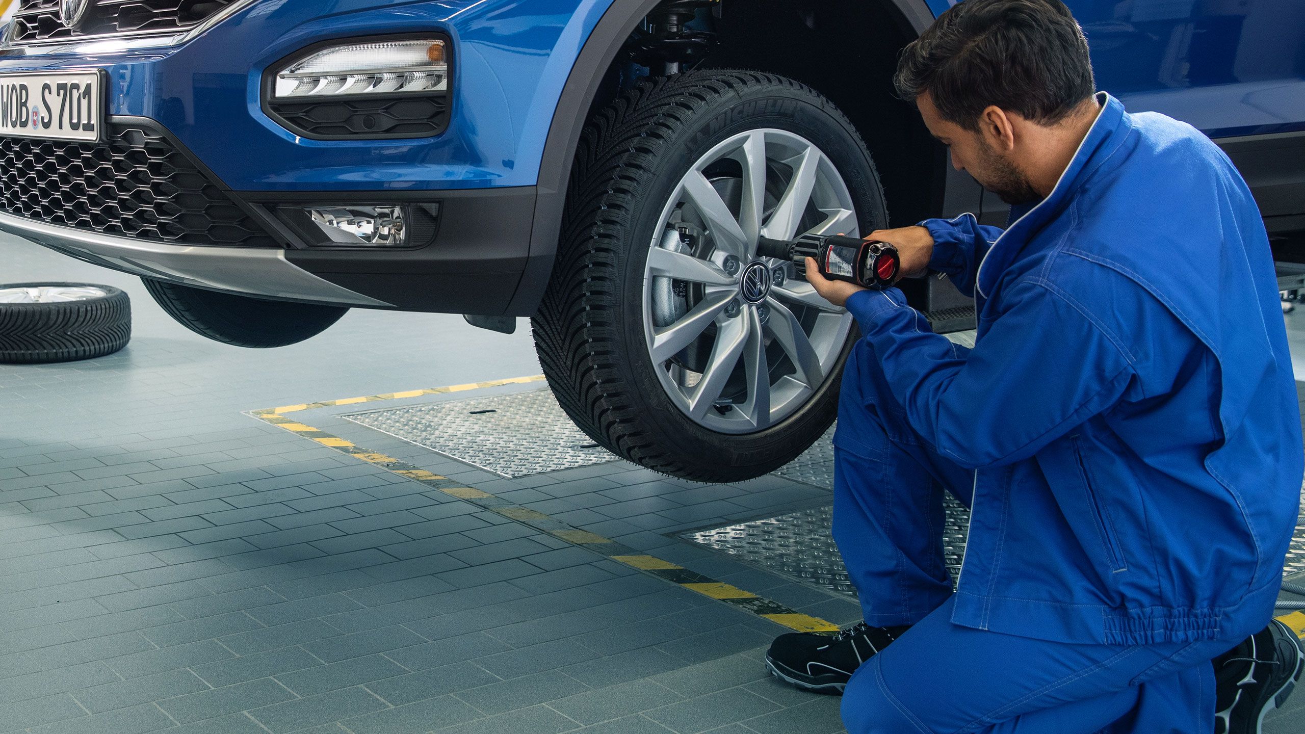 Um empregado de serviço da VW fixa a roda após a mudança da roda do carro azul da VW numa oficina