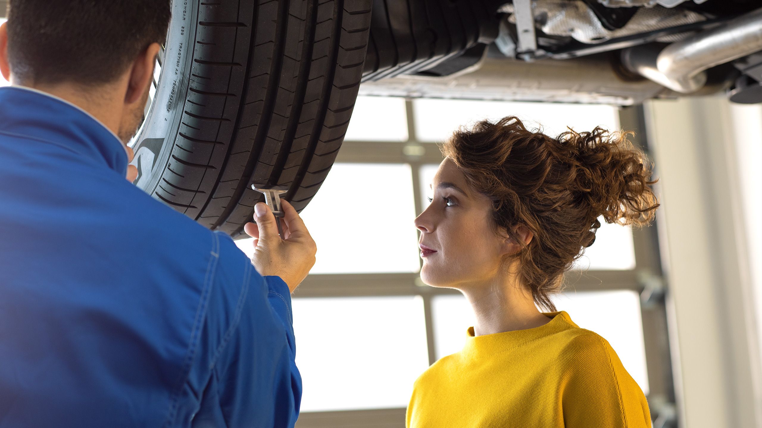 Um empregado de serviço da VW fixa a roda após a mudança da roda do carro azul da VW numa oficina