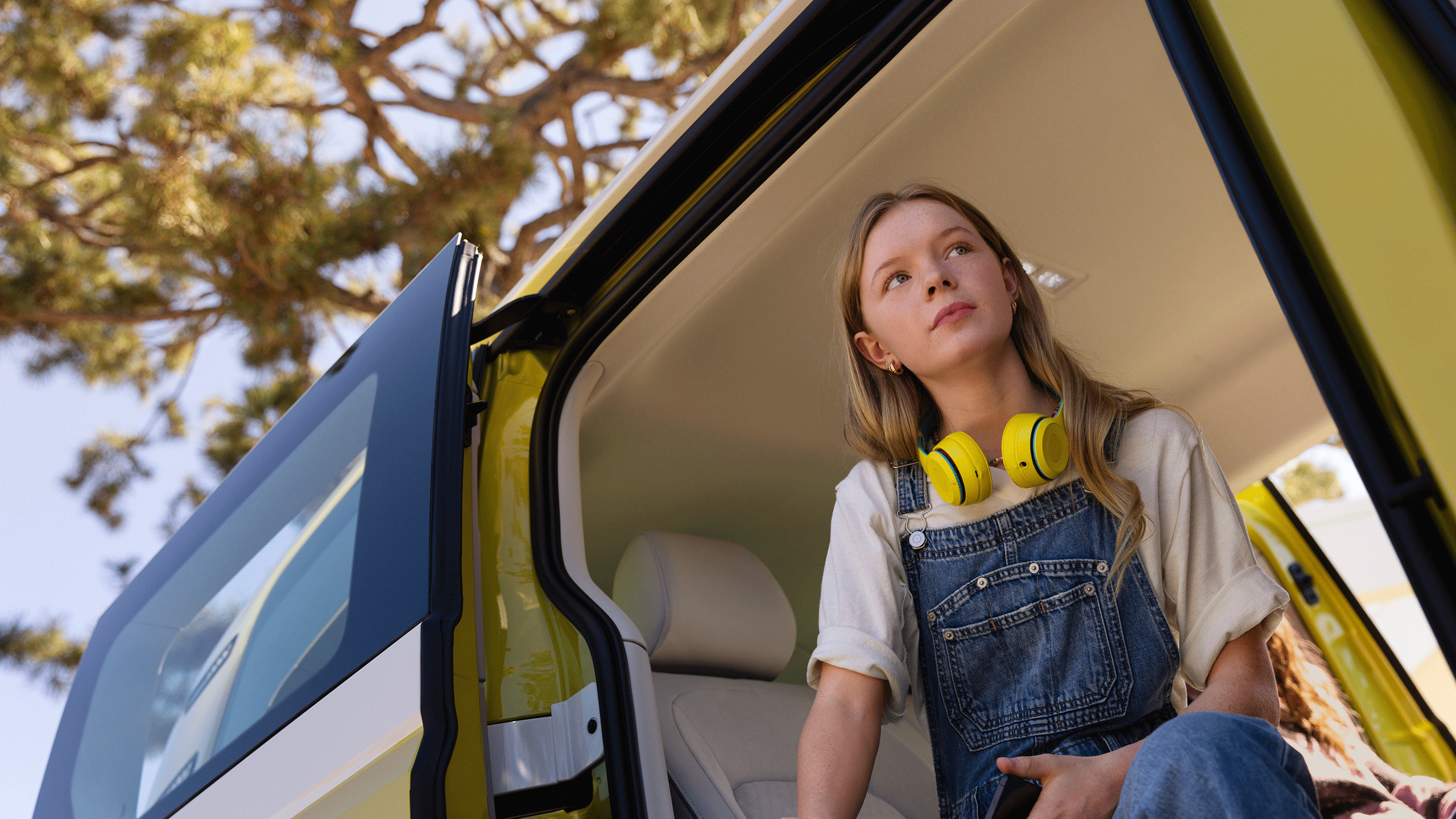 Um rapariga com auriculares amarelos sentada na porta lateral do VW ID. Buzz.