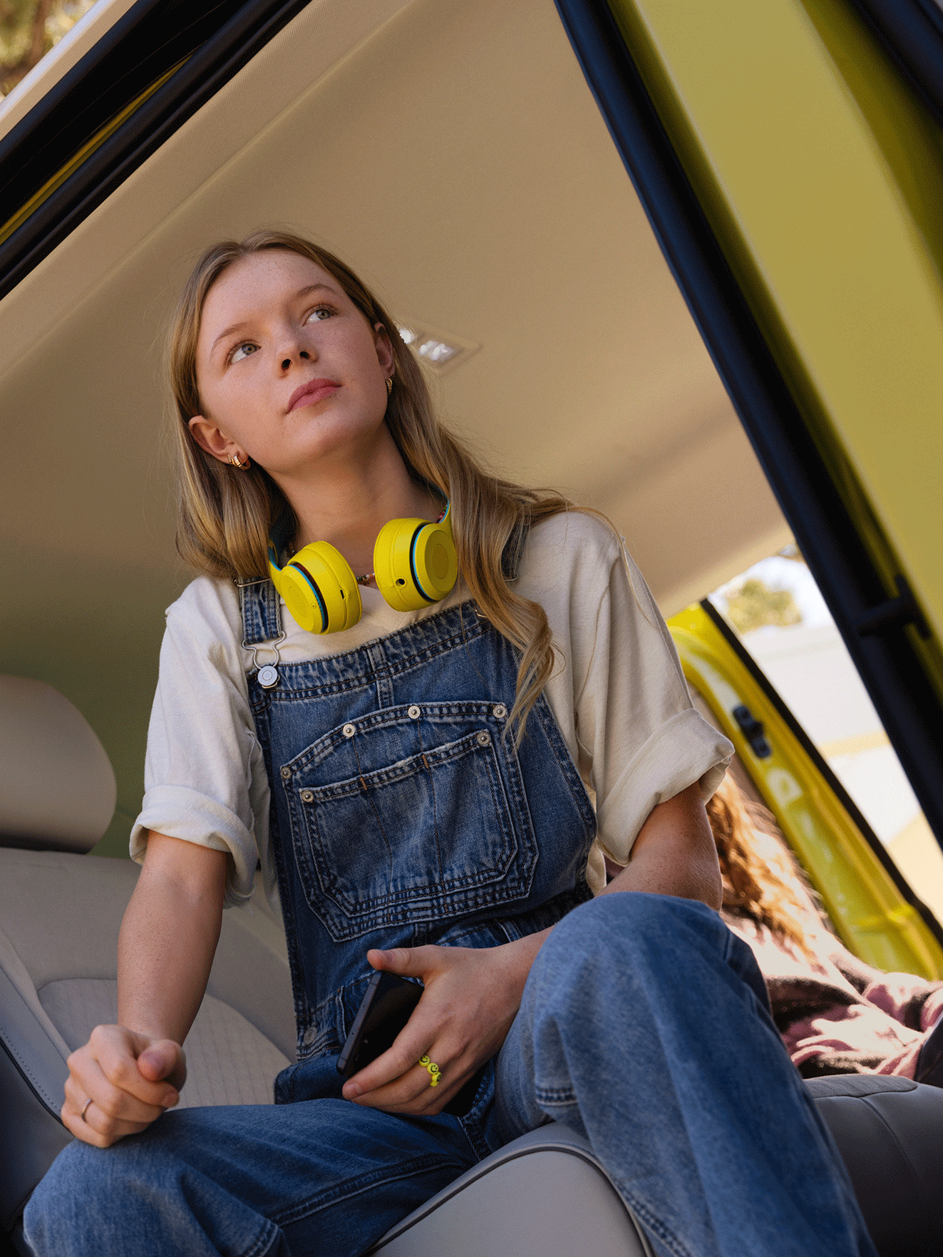 Um rapariga com auriculares amarelos sentada na porta lateral do VW ID. Buzz.