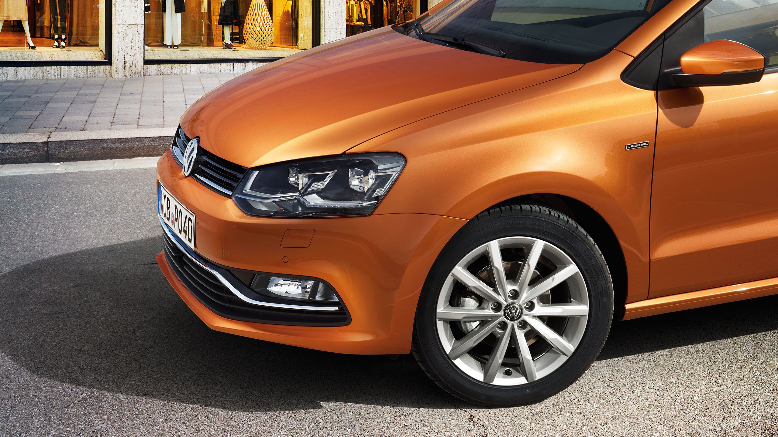 A vista lateral de uma Volkswagen Polo 5 laranja em frente a uma loja