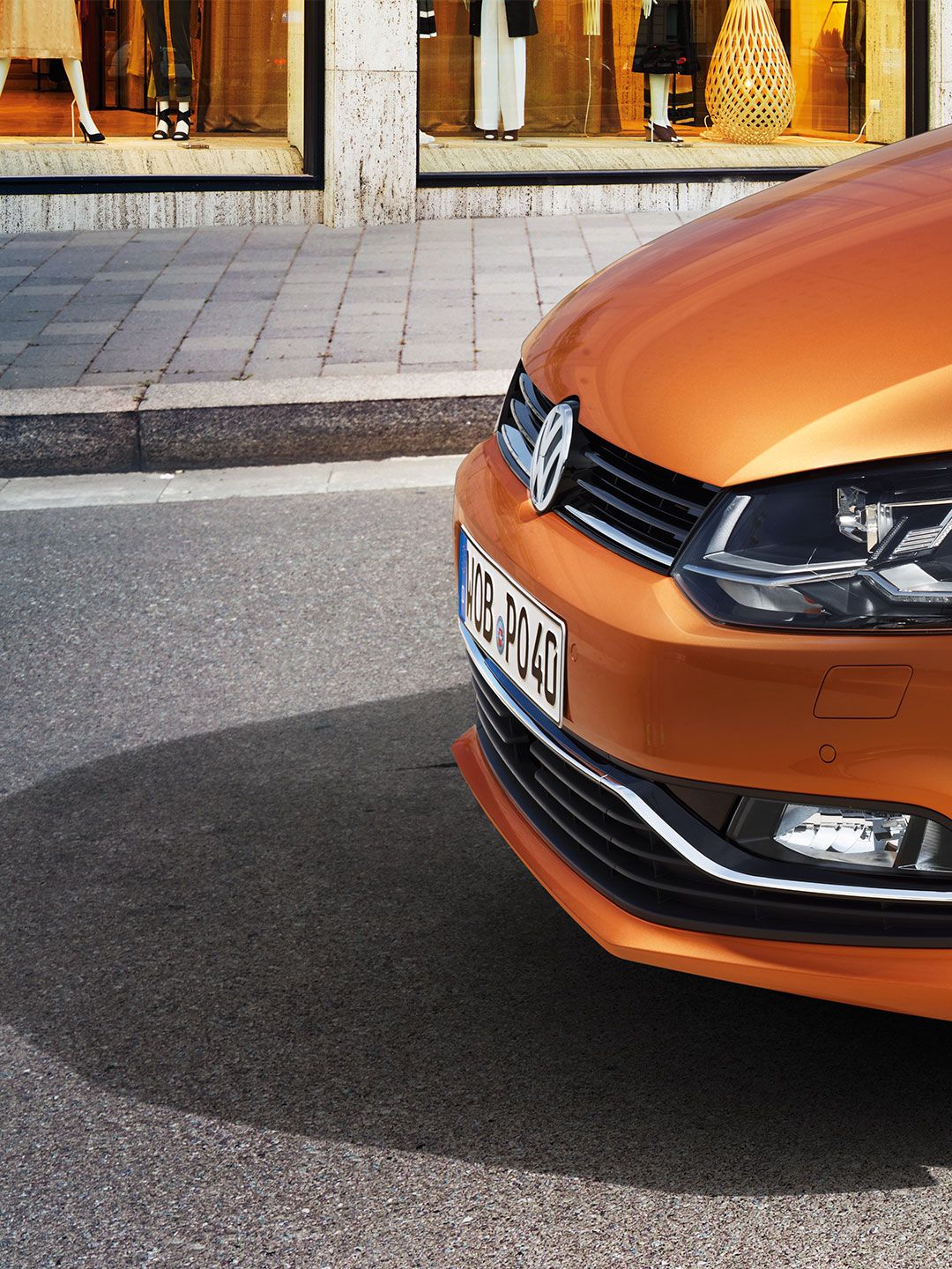 A vista lateral de uma Volkswagen Polo 5 laranja em frente a uma loja