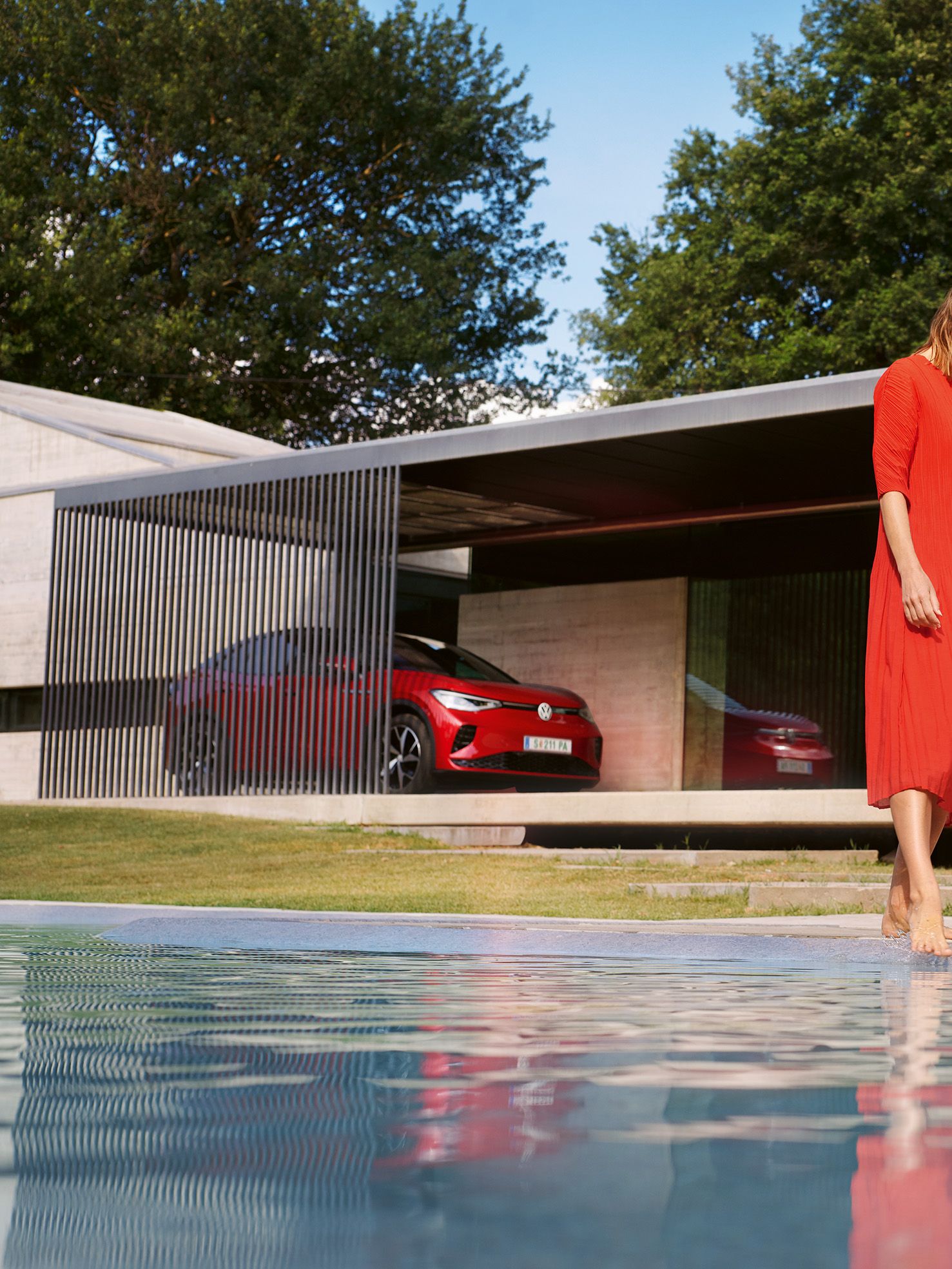 VW ID.5 GTX vermelho a estacionar em frente de uma casa. Mulher de vestido vermelho junto à piscina.