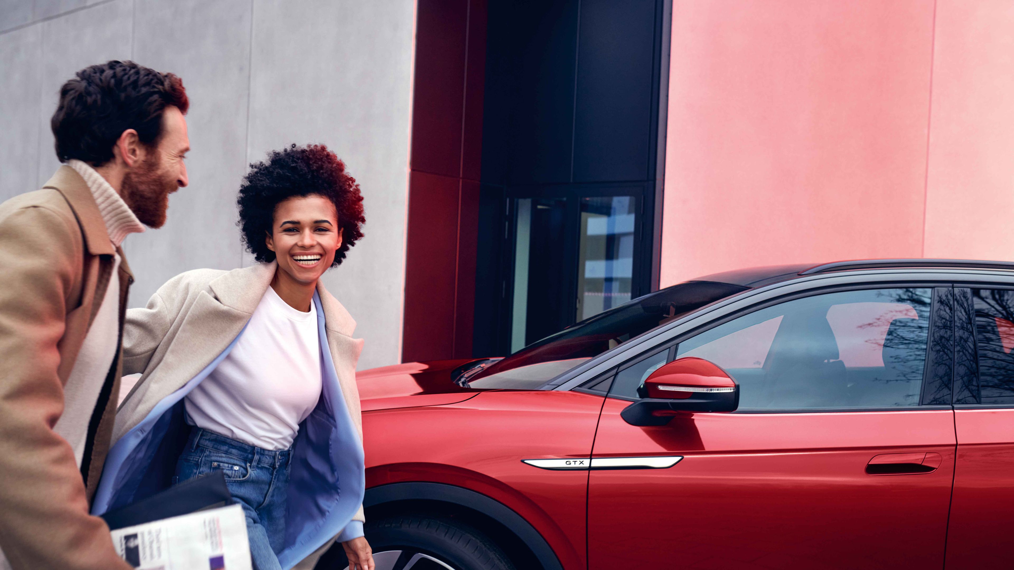 VW ID.4 GTX em vermelho na berma da estrada. Homem e mulher caminham sorridentes.