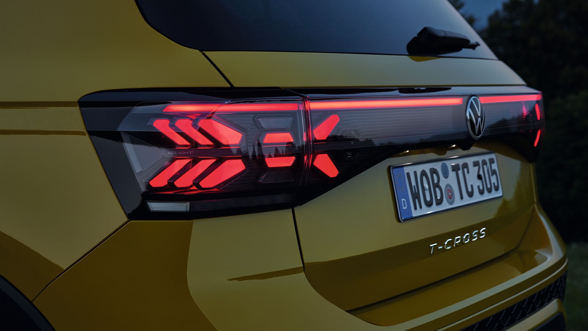 Iluminação traseira de um VW T-Cross amarelo em grande plano ao crepúsculo.