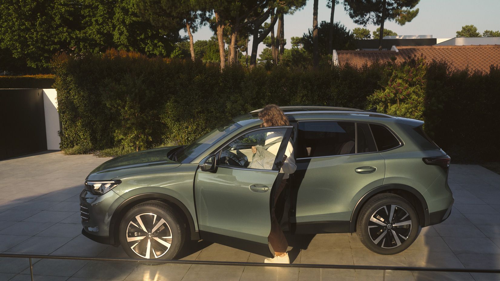 VW Tiguan verde escuro estacionado numa entrada, uma mulher entra do lado do condutor.