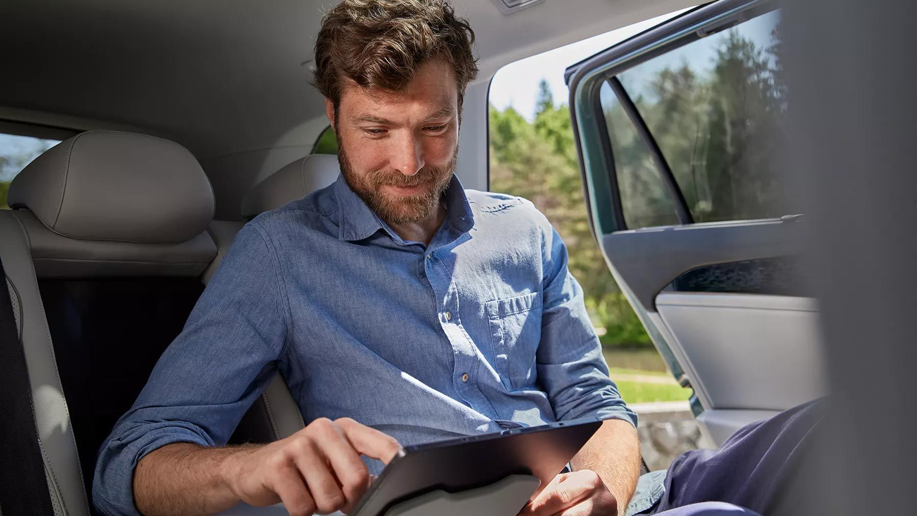 Um homem no banco traseiro do VW Passat colocou o seu tablet no suporte do apoio de braços central. 