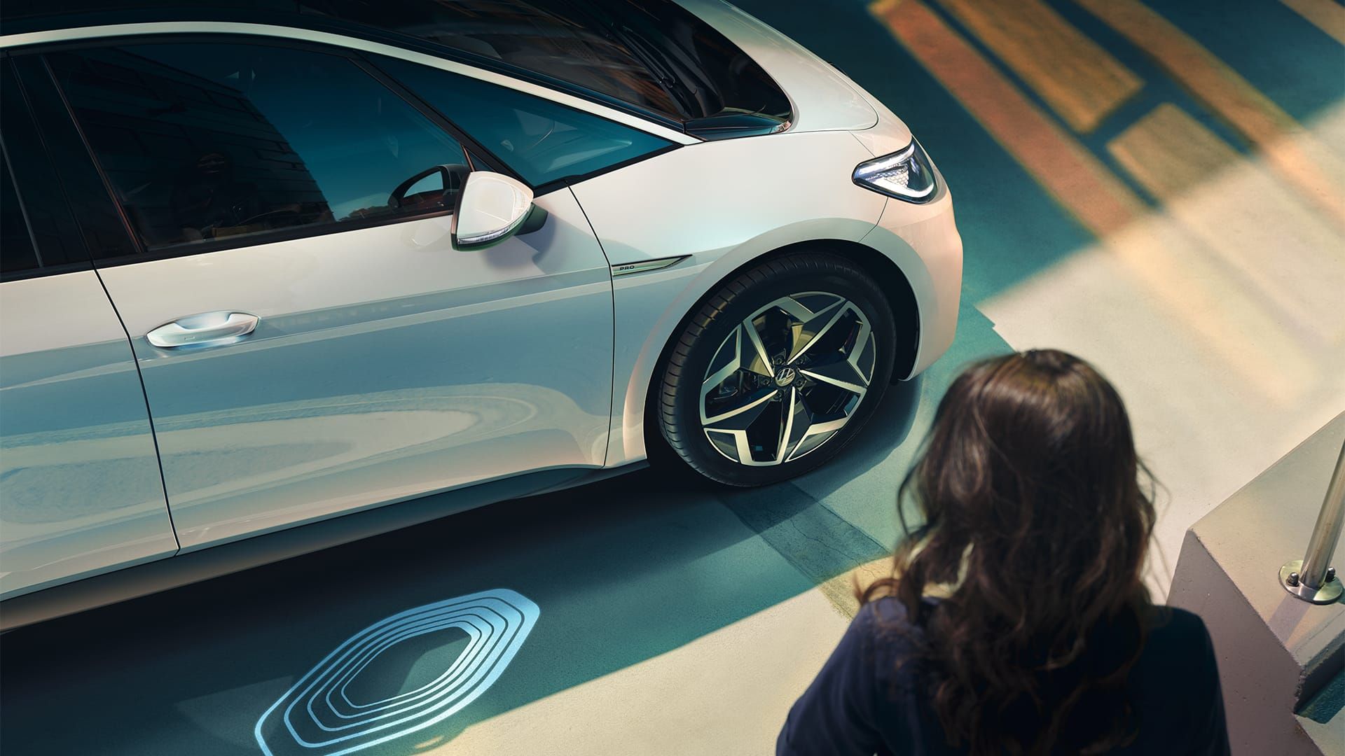 VW ID.3 em branco, visível de lado, mulher a dirigir-se para o veículo, projeção de logótipos em foco