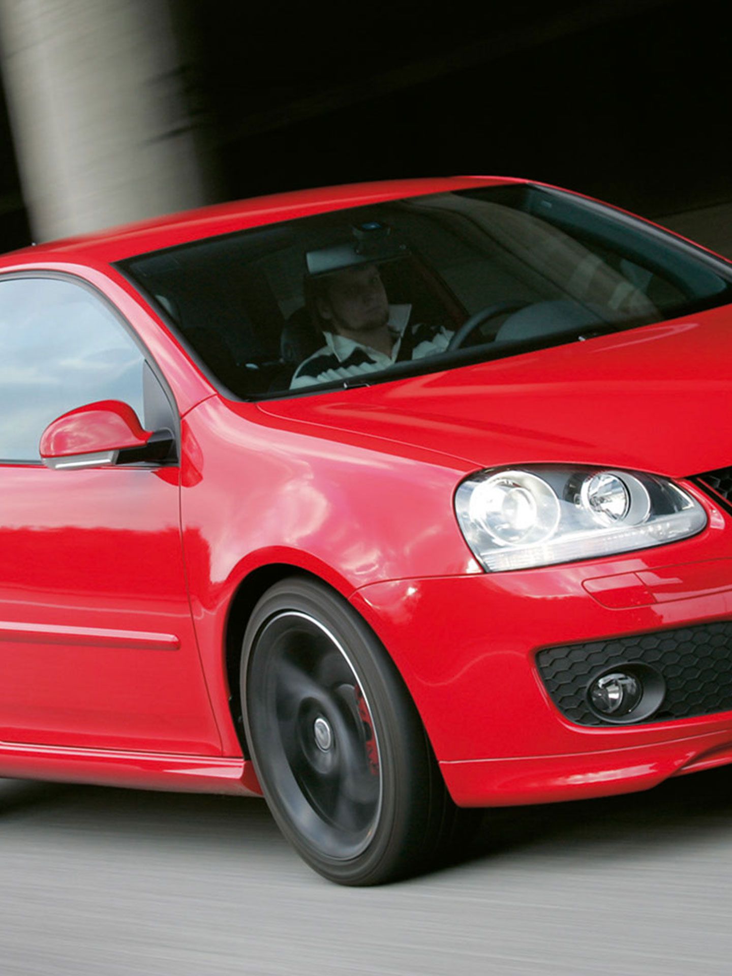 Um homem conduz num VW Golf V GTI vermelho